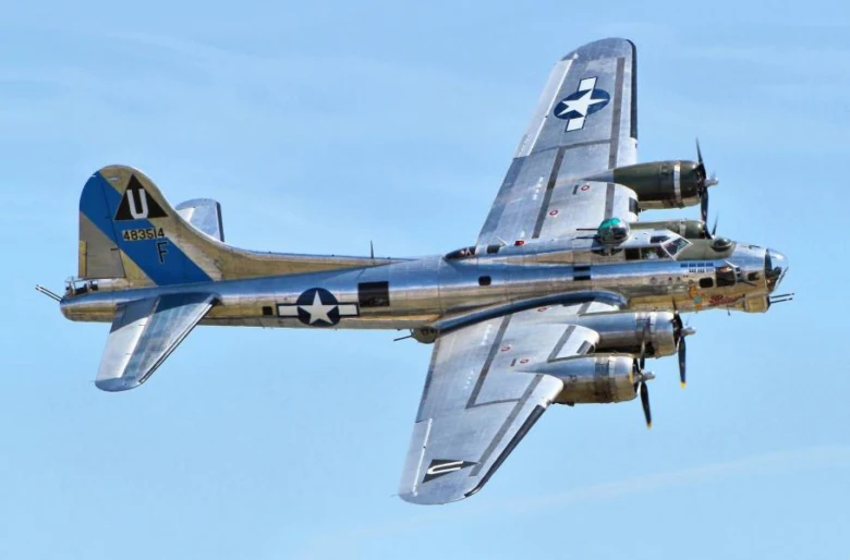 Stříbrný americký bombardér B-17 v letu na modré obloze.