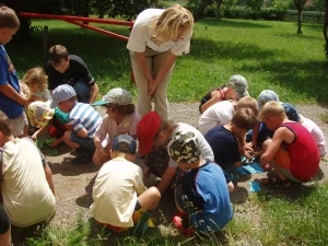Děti sedí na trávě s učitelkou v přírodě.