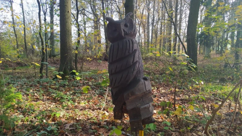 Dřevěný sova stojí v lese mezi stromy.