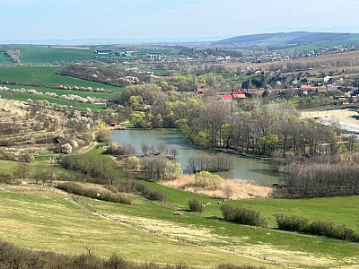 Přírodní rybník v krajině s okolními poli a vesnicí