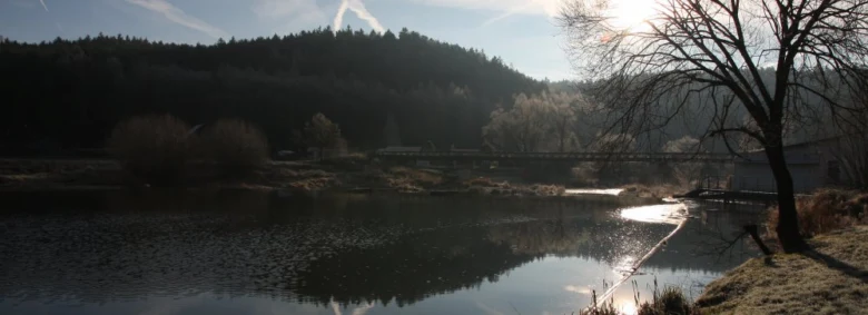 Řeka v krajině s lesy a kopci pod sluncem.