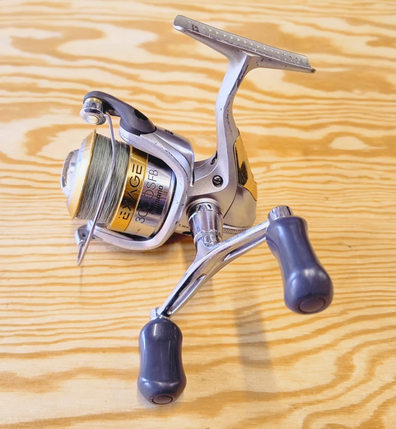 Stříbrný rybářský naviják značky Shimano na dřevěném stole.